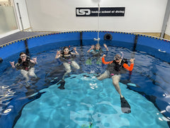 Divers smiling underwater in the heated indoor pool at London School of Diving